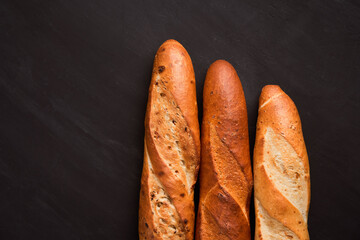 Three crispy french baguettes lie on an old wooden table with free space for text