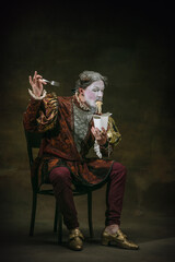 Eating instant noodles. Young man as Johann Bach isolated on dark green background. Retro style, comparison of eras concept. Beautiful male model like historical character, great music composer, old