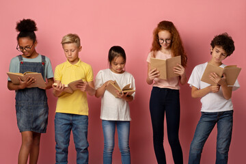 Industrious diverse children reading school textbooks on pink background