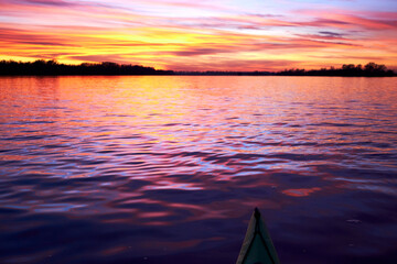 Bow of green kayak at colorful sunset over Danube river at autumn time