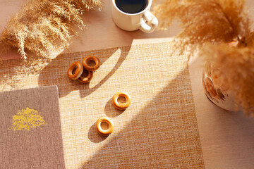 A cup of coffee, dry flowers, barankis, notepad on wooden table.