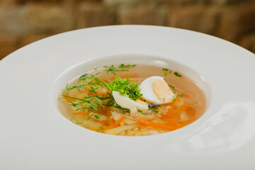 Fresh soup with vegetables, meat and eggs in a white plate.