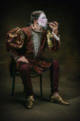 Eating an oyster. Young man as Johann Bach isolated on dark green background. Retro style, comparison of eras concept. Beautiful male model like historical character, great music composer, old