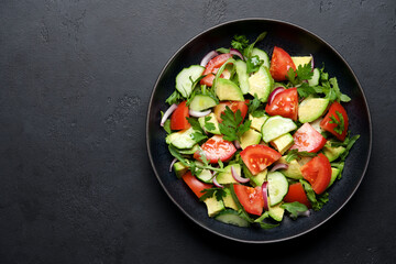 Avocado salad with tomatoes, cucumbers, parsley and arugula. Balanced nutrition concept. Black stone background