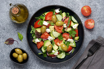 Greek salad with avocado. Tomatoes, cucumbers, olives, feta cheese fresh ingredients. Black background, top view