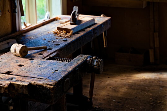 Carpenters workshop with tools and woodcarvings strewn on the table and natural sunlight streaming in.