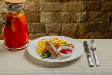Freshly fried kebab with fried potatoes and tomato sauce on a white plate.