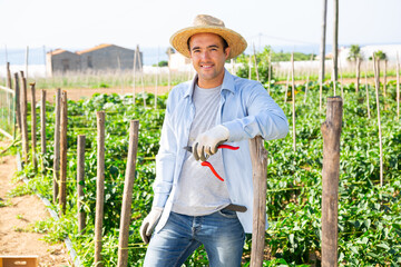 Cheerful amateur gardener in wicker hat posing in farm backyard in summer