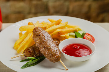 Freshly fried kebab with fried potatoes and tomato sauce on a white plate.