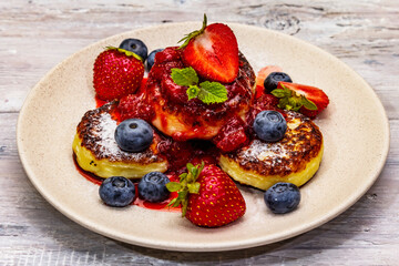 Cottage cheese pancakes with fresh berries and strawberry sauce. Healthy breakfast concept on wooden background