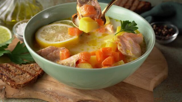 Stiring delicious salmon creamy soup with carrots and potato in a green plate. Close up. 4K UHD