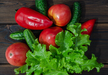Tomatoes, cucumbers, zucchini, bell peppers, lettuce on a wooden background close-up.