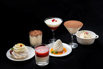Pavlova meringue cake with fresh berries on black background. Decorated with a berry and a mint leaf. Various desserts are in the background.