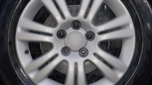 A car wheel with a shiny silver rim rides in the rain drops, turns to the right, to the left and strong shaking on bad road. Closeup. Slow mo, slo mo, slow motion, high speed camera