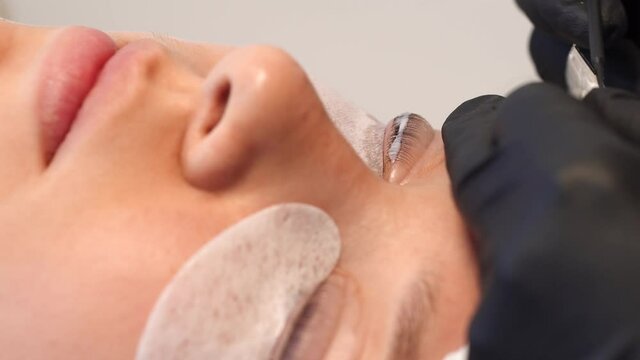 Closeup view 4k video of female face of young girl and professional cosmetologist doing modern spa cosmetic procedures of lashes lamination.