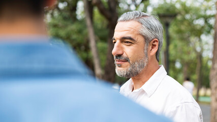 Portrait of handsome Caucasian older man talking with friend or his son at park, senior father give...