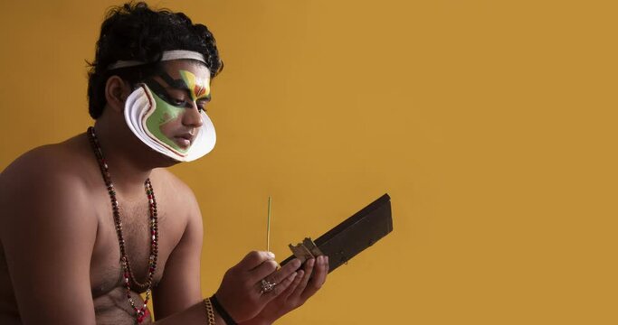 Kathakali artist doing pacha make up on his face while looking in the mirror	