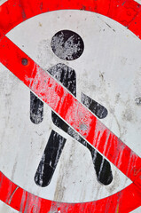 A red-and-white sign, smeared with paint, dirt, and cracks - a person is not allowed to pass.