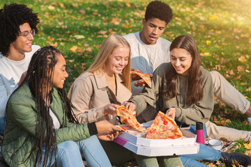 Hungry teen friends eating pizza at public park