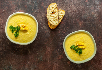 Plates with autumn spicy corn soup and ingredients. Served with corn cobs, greens, bread. Vegetarian recipe
