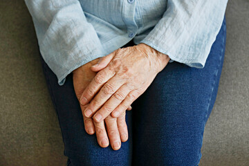 Elderly woman sitting alone at home, with hands folded on her laps. Senior old lady experiencing...