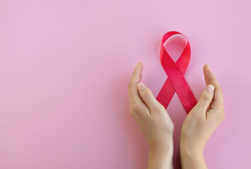 Breast cancer awareness concept. Womans hands hold pink ribbon on light background. Close up, top...
