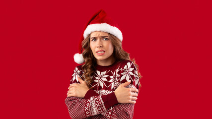 Unhappy young girl in Christmas outfit shivering from cold over red background