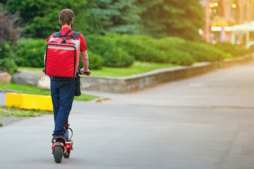 Courier deliver food on electric scooter. Boy delivering hot food to costumers. Delivery man deliver fresh hot food, rides fast on an electric scooter. Delivery service from cafes and restaurants.