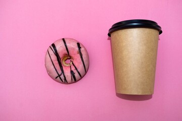 Coffee in a paper cup with a donut on a pink background. Top view. Empty space for design
