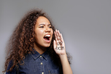 Portrait of young beautiful black woman showing a stop racism slogan written on palm of her hand....