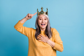 Closeup portrait photo of charming elegant funny senior lady crown head pointing fingers laughing open mouth love herself concept wear yellow jumper bright blue color background © deagreez