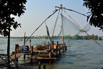 Fototapeta premium Stationary Chinese fishing nets (“Cheena vala” in Telugu) or shore operated lift nets seen through the trees at the sunset in Kochi Fort, Cochin, India
