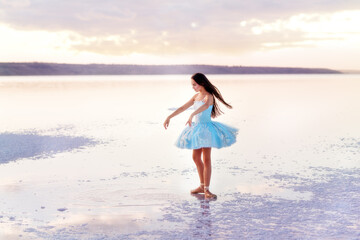 Fototapeta na wymiar Girl ballerina in a ballet dress dances in the water of the lake at sunset.