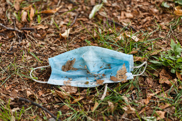 A dirty Used Disposable Medical Mask is lying on the ground. Environmental disaster due to disposable masks