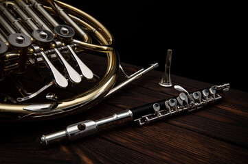 Two musical instruments French horn and flute on a wooden surface on a black background
