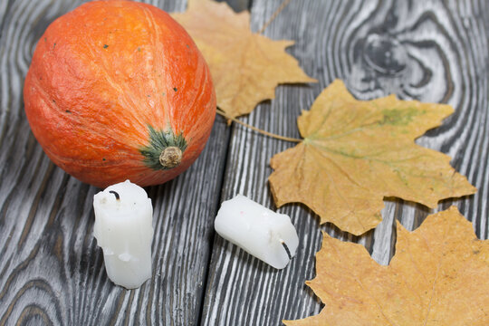 Orange pumpkin and candle stubs. Nearby maple leaves. On brushed pine boards painted black and white.