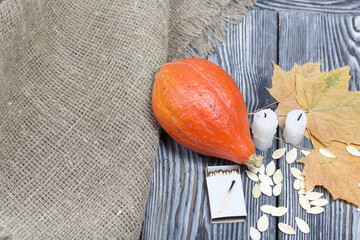 Orange pumpkin, seeds and candle stubs. Nearby are boxes of matches and dried maple leaves. On brushed pine boards painted black and white.