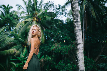 Seductive blonde female standing by exotic trees