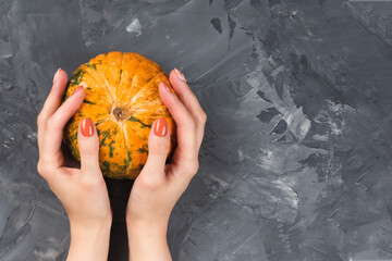 Woman holds a pumpkin. Female hands with trendy autumn marble manicure in orange color. Flat lay, copy space for your text
