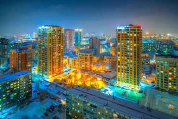 Fototapeta na wymiar Beautiful top view of the city. Colorful street lighting of the night metropolis. Many high-rise buildings. Cold winter weather. There is snow on the roofs of houses. Novosibirsk, Siberia, Russia.