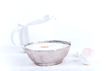Silver bowl with full of milk and egg yolk on a white background with a white creamer, isolated, close up 