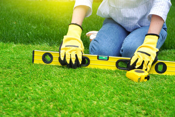 Woman sits on the green artificial grass and holds a water level