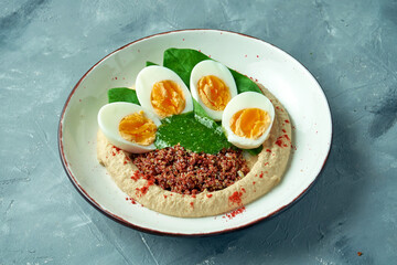 Healthy food - hummus with quinoa, spinach and boiled egg in a white bowl on a gray background