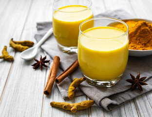 Yellow turmeric latte drink. Golden milk with cinnamon, turmeric, ginger  and honey over white marble background.