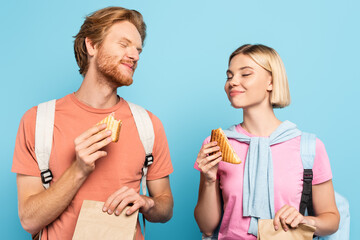 young students with closed eyes holding paper bags and sandwiches on blue