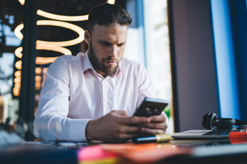 Serious businessman browsing smartphone in workplace