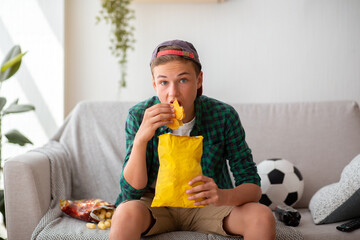 Teenager watching football game and eating unhealthy food