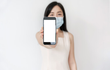 Asian woman showing mobile smart phone with blank white screen, and wearing medical face mask 