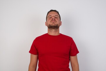 Obraz premium Young caucasian man wearing red t-shirt over white background looking sleepy and tired, exhausted for fatigue and hangover, lazy eyes in the morning.