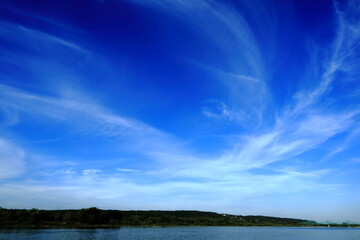 Wide landscape with deep blue sky and wispy cirrus clouds over a calm lake and forest horizon. A peaceful and open natural scene ideal for backgrounds or nature-themed projects